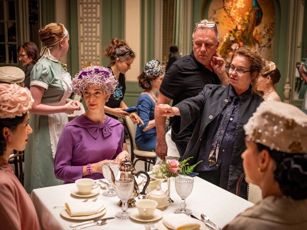 An image of women sitting at a table wearing clothing from the 1950s. A woman points at the costumes giving direction for adjustments.