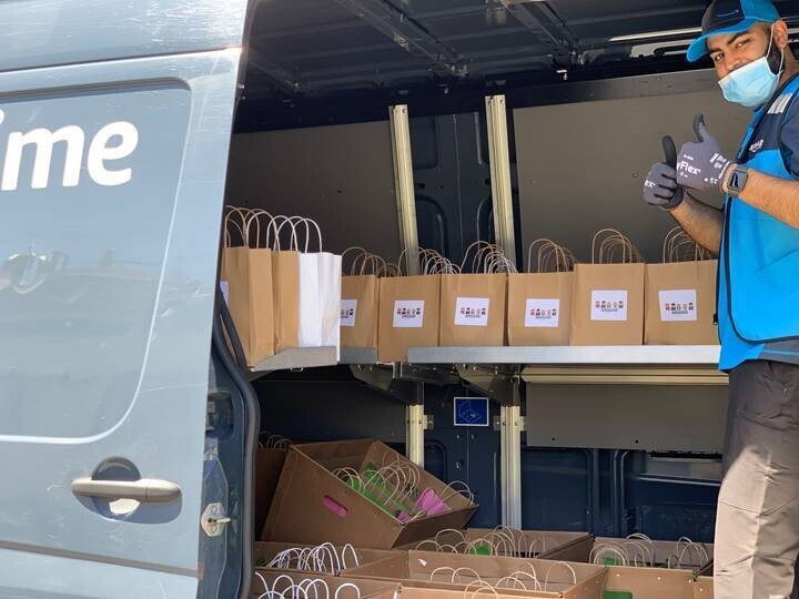 A delivery driver gives a thumbs-up sign while standing in a van filled with bags to be delivered.