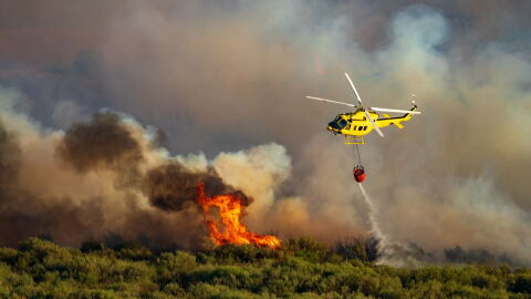 Image of a helicopter dropping water over a forest fire 