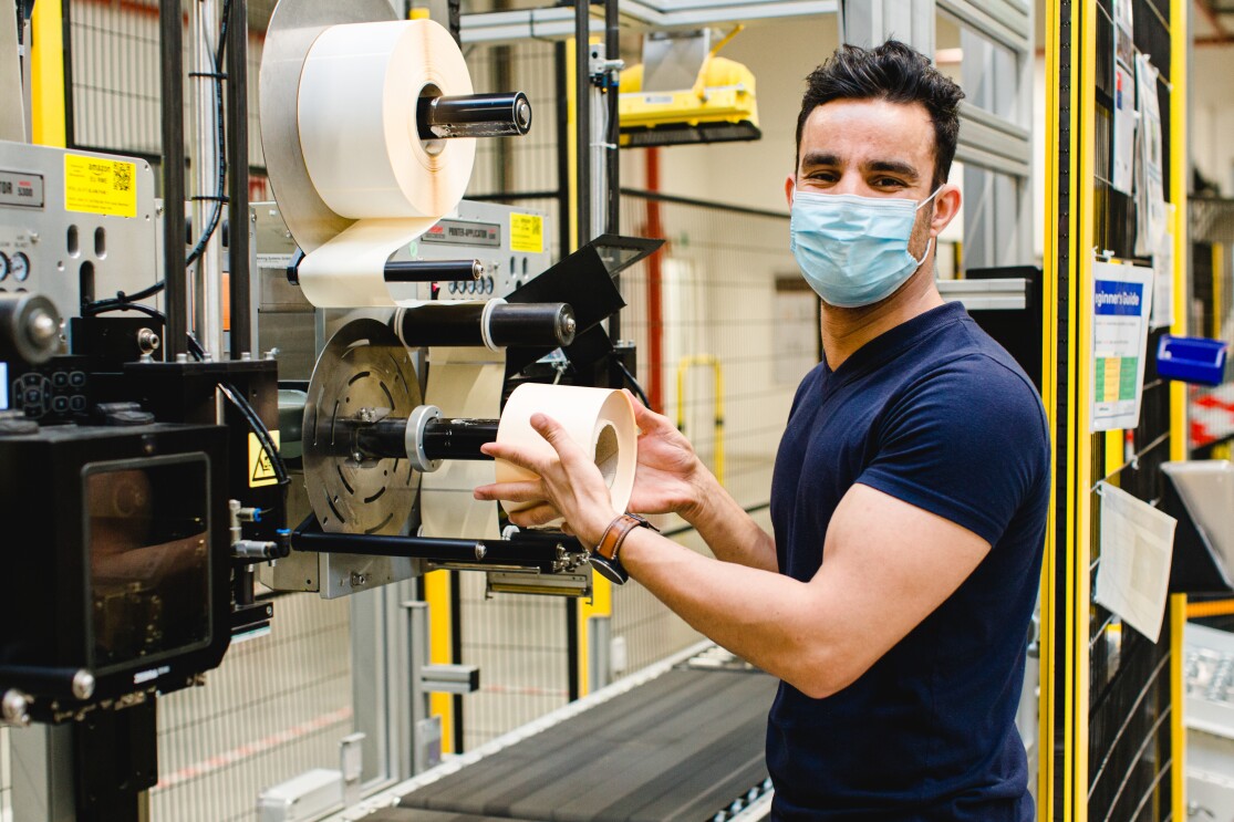Ein junger Mann mit Maske an einer Etikettiermaschine