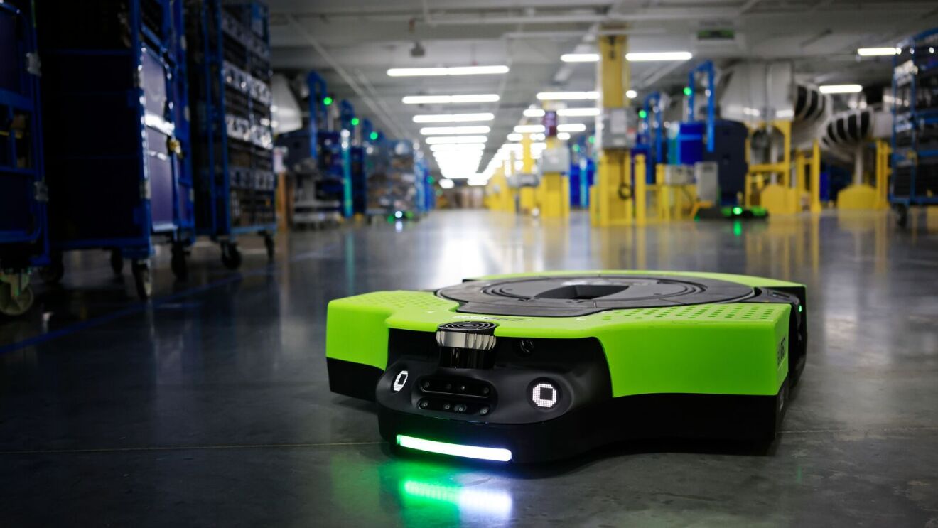 Sleek green robotic transporter named Proteus in brightly lit Amazon fulfillment center