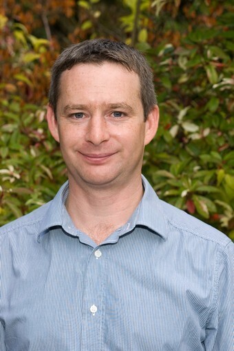 Richard Kneller dressed in a blue shirt looking directly at the camera
