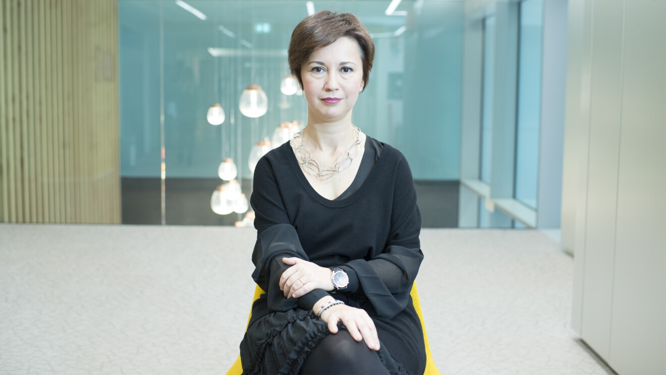 Mariangela Marseglia, directora General de Amazon España e Italia. En un espacio con una silla de color amarillo y un armario color blanco, aparece sentada en esa silla Mariangela Marseglia. Con el pelo corto de color castaño, tiene los brazos cruzados, e una muñeca tiene un reloj y en la otra una pulsera. Va con un vestido negro por la rodilla y encima un jersey negro de manga corta y de punto. Tiene un collar de piezas ovaladas unidas. De fondo se ve un cristal y una lámpara colgando del techo y que parece que da a un hall amplio. Si bien una de las paredes es un armario, la otra son unos tableros verticales de madera. 