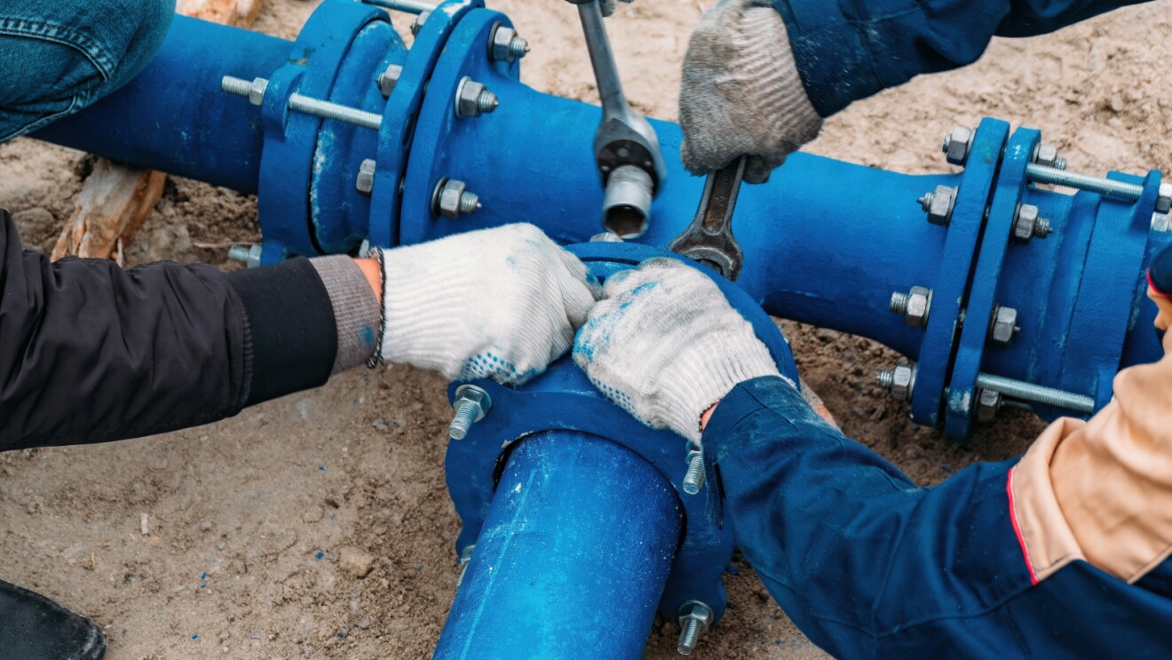 Workers installing a blue pipe joint with bolted flanges