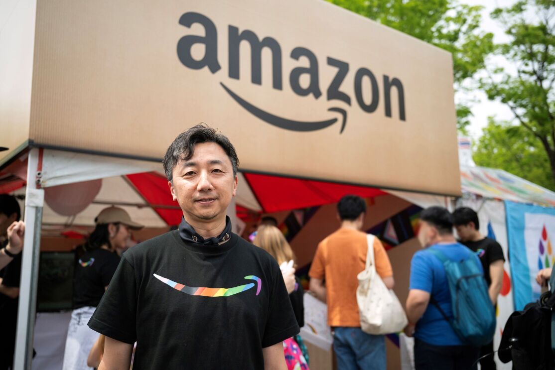 Amazonと書かれたブースの前に立つ男性。黒いTシャツを着ている