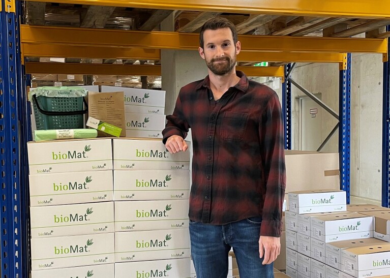 EIn Mann mit einem karierten Hemd steht in einer Lagerhalle neben einem Stapel bioMat-Kartons.