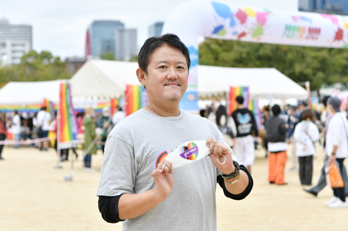 レインボーのハートとglamazonが書かれたマスクを見せてくれる倉橋さん