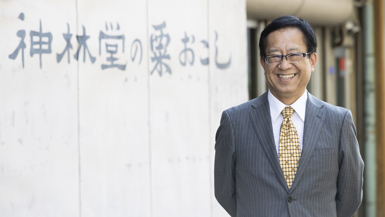 『神林堂の粟おこし』の文字を背景に笑顔の岸本さんの写真
