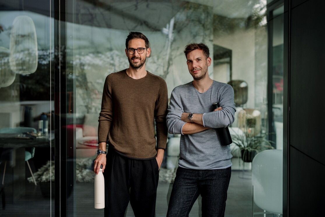 Sebastian und Patrick stehen in ihrem Büro und halten Produkte (Wasserflaschen) in der Hand