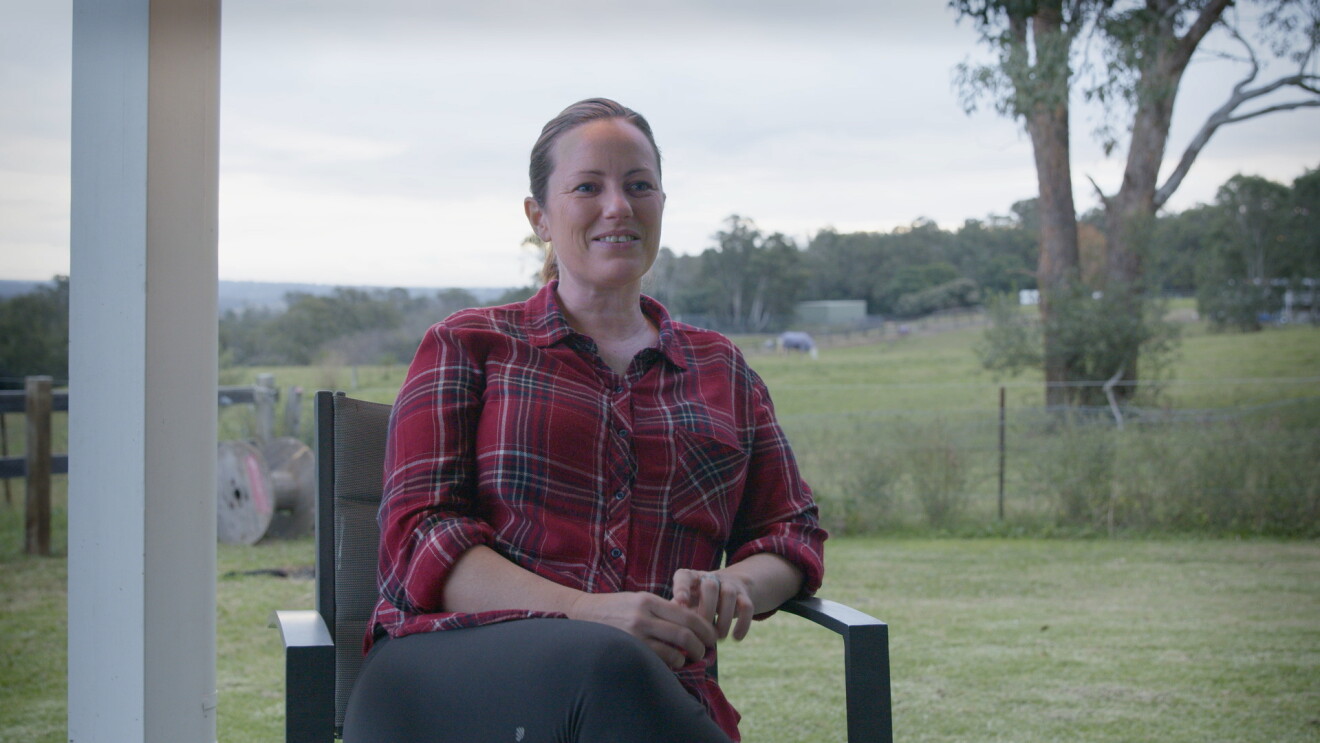 Tanya sits on a porch outside, looking toward the interviewer just off camera.