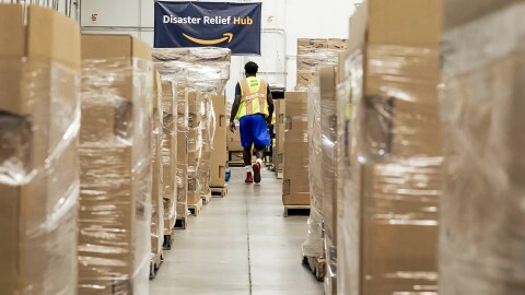 Un dipendente Amazon in un corridoio di scatoloni e pallet. Sulla parete di fondo, una bandiera con la scritta "Disaster Relief Hub"