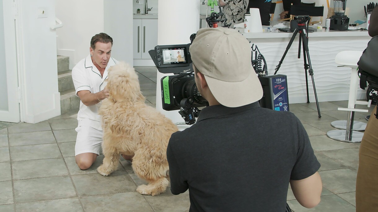 An image of a person filming Carlos Ponce petting a dog behind the scenes of Amazon's miniseries “Living La Vida Prime.”