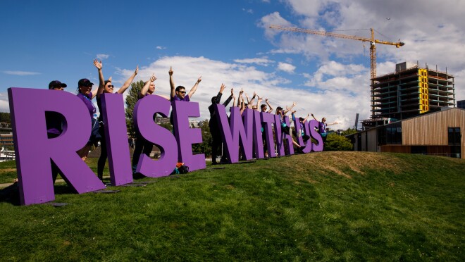 “崛起”与我们签署美国特奥会,设置在一个山坡上在西雅图。紫色的字母显示有超过一打亚马逊员工志愿者挥手和微笑,因为他们欢迎运动员闭幕式。