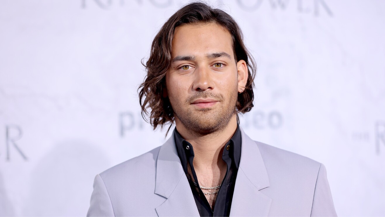 an actor from the lord of the rings the rings of power stands for a photo on the red carpet of the premiere.