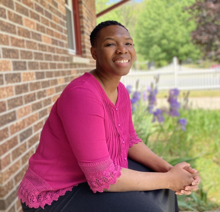 Moalyne Honore wears a pink blouse and smiles as she sits on a step outside of her home.