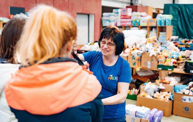 Ukraine Hilfe der Arche in Berlin Community Fund. Mitarbeiterin der Arche verteilt Spielzeugspenden an Kinder. Im Hintergrund sind weitere Kisten mit Spielzeug erkennbar.
