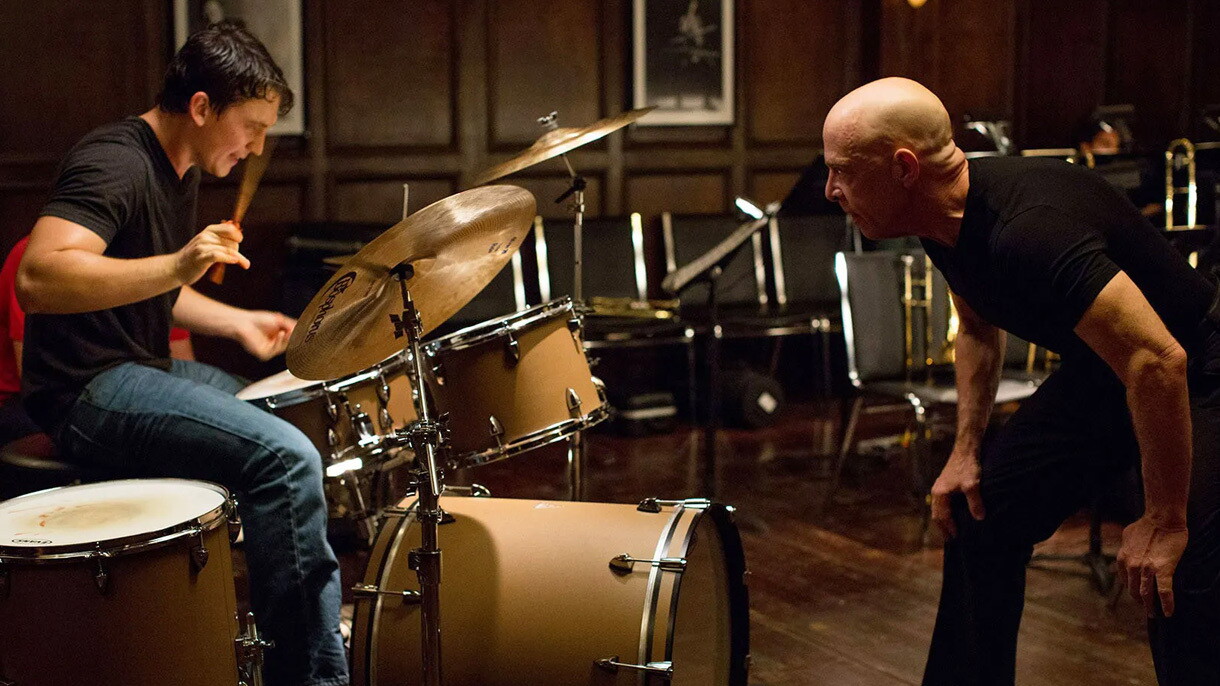 A scene from the movie whiplash where a man stares at another man as he plays the drums.