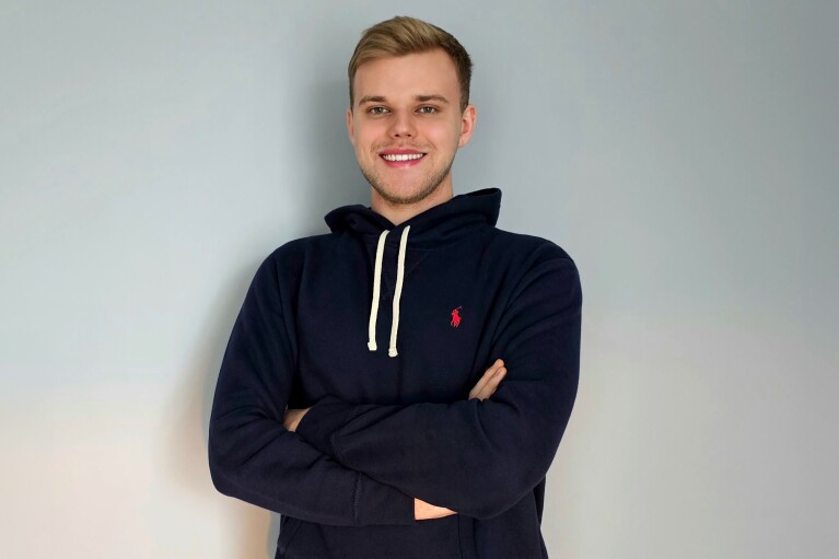 A young man stands in front of a blue background
