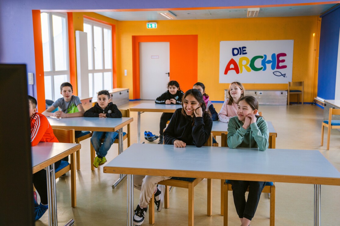 Kinder der Arche sitzen in einem Klassenzimmer und verfolgen die virtuelle Tour auf einem Bildschirm. Sie lachen, haben sichtlich Spaß.