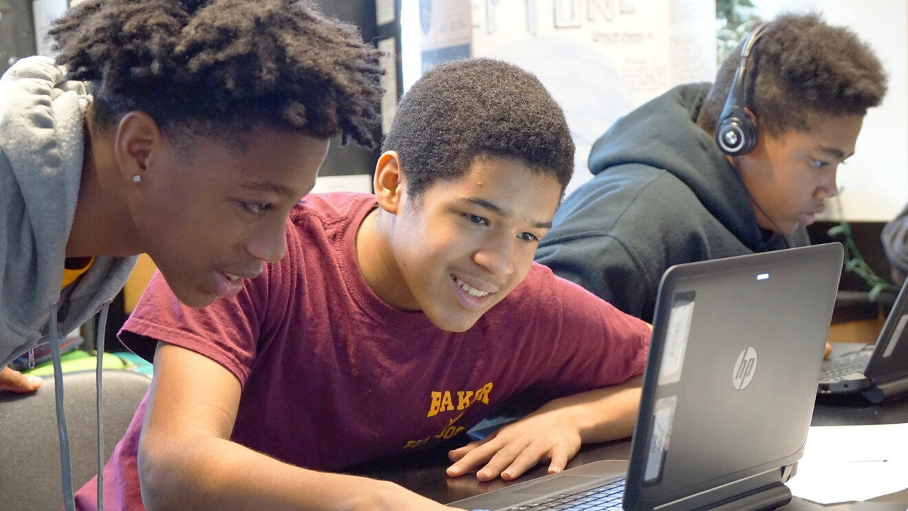 Students use a laptop in a classroom while working together on a coding project.