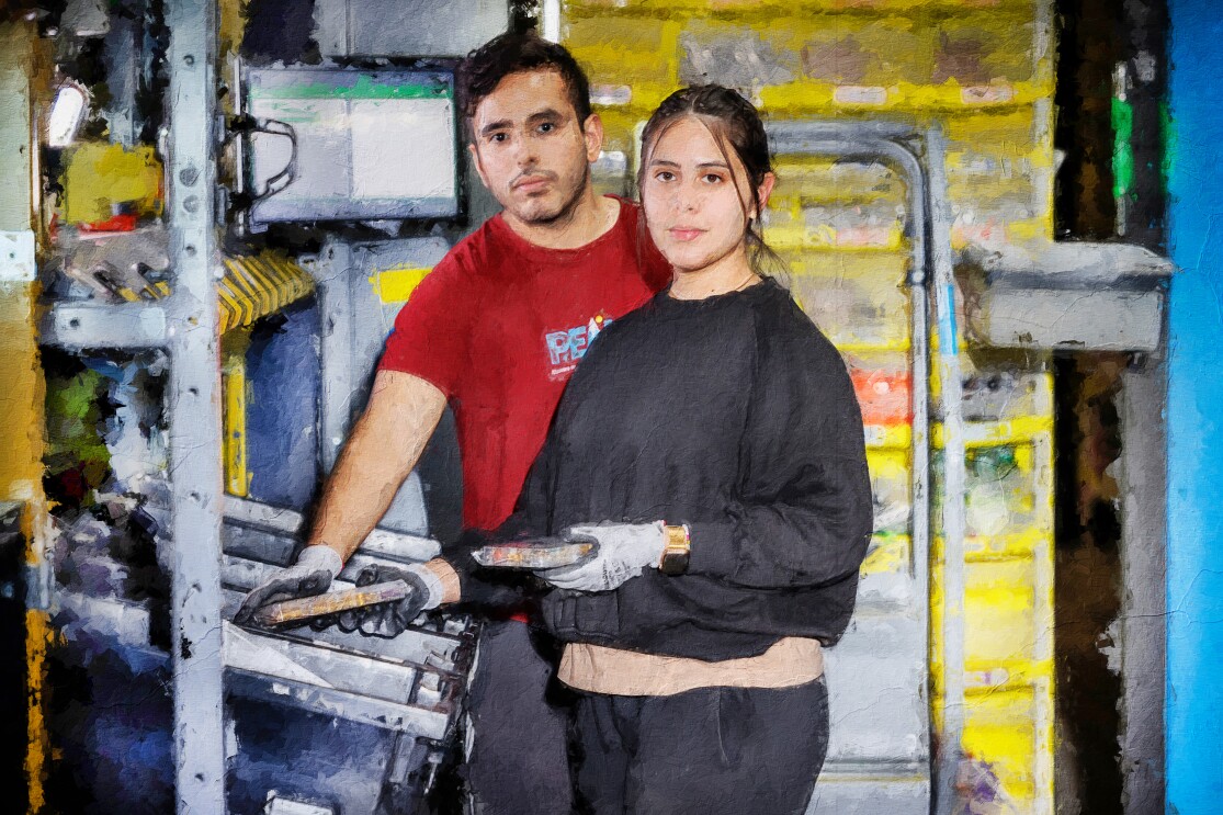 Fotomontaje. Es una fotografía que lleva un filtro que simula un cuadro pintado. En él aparecen una estantería amarilla y están delante de un ordenador y de una caja en el que están preparando pedidos. Aparece un hombre y una mujer, los dos con un objeto en la mano. La mujer está en primer plano vestida con un chándal negro y con el pelo marrón recogido. Detrás de ella aparece un hombre con camiseta roja.