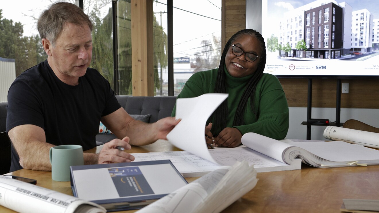 A photo of two people sitting at a desk reviewing blueprints.