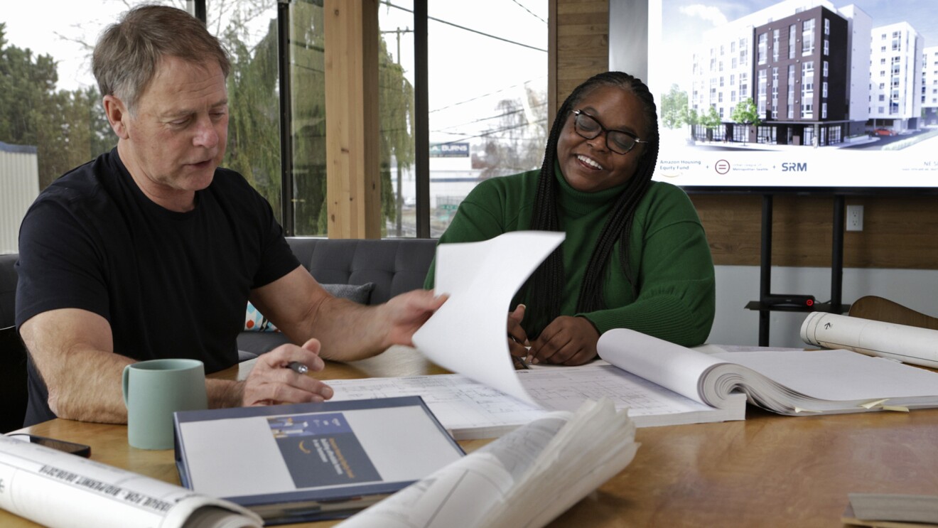 A photo of two people sitting at a desk reviewing blueprints. 