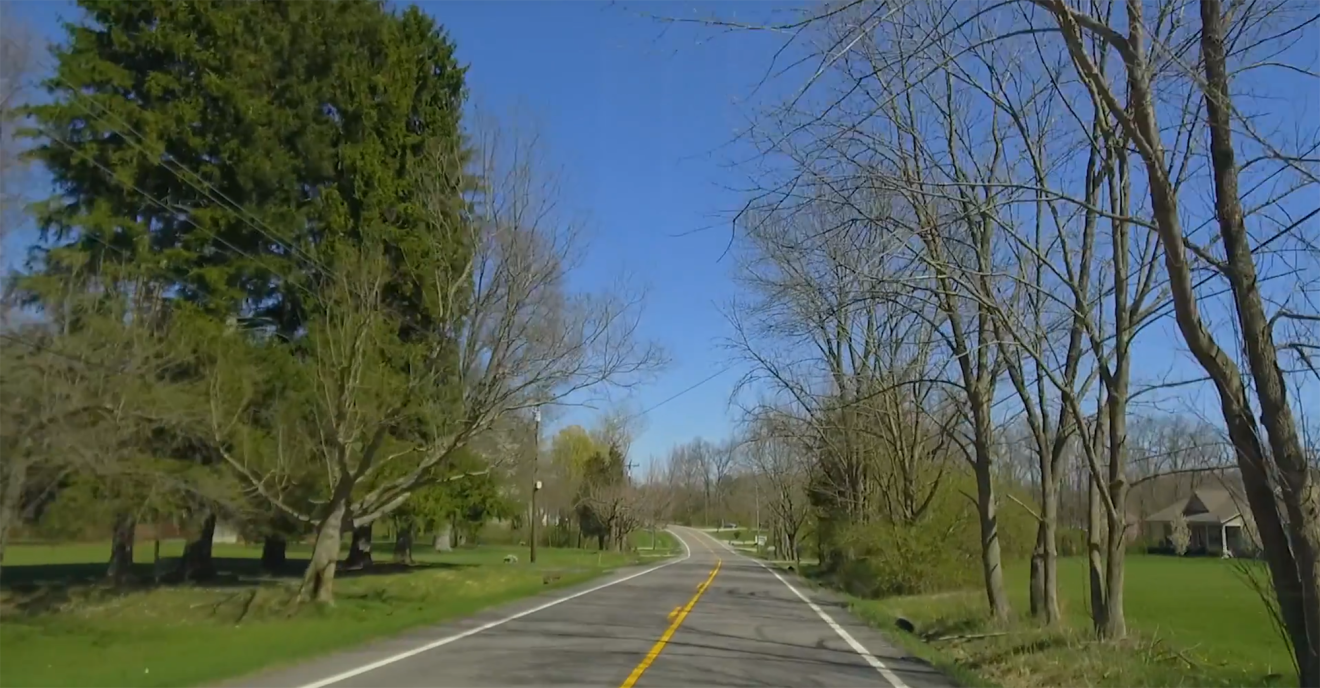Ohio countryside with a two-lane road running through trees and rolling lawns.