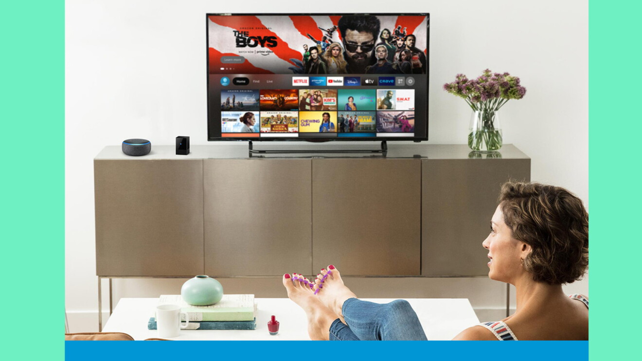 A woman sits on a sofa in a living room and looks at a TV