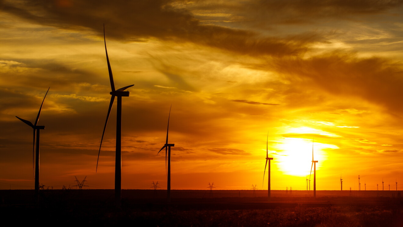 PLana de energía eólica de Texas, EE.UU. Una puesta de sol en un campo con molinos de viento. El cielo es rojo y amarillo y los molinos aparecen de color negro. 