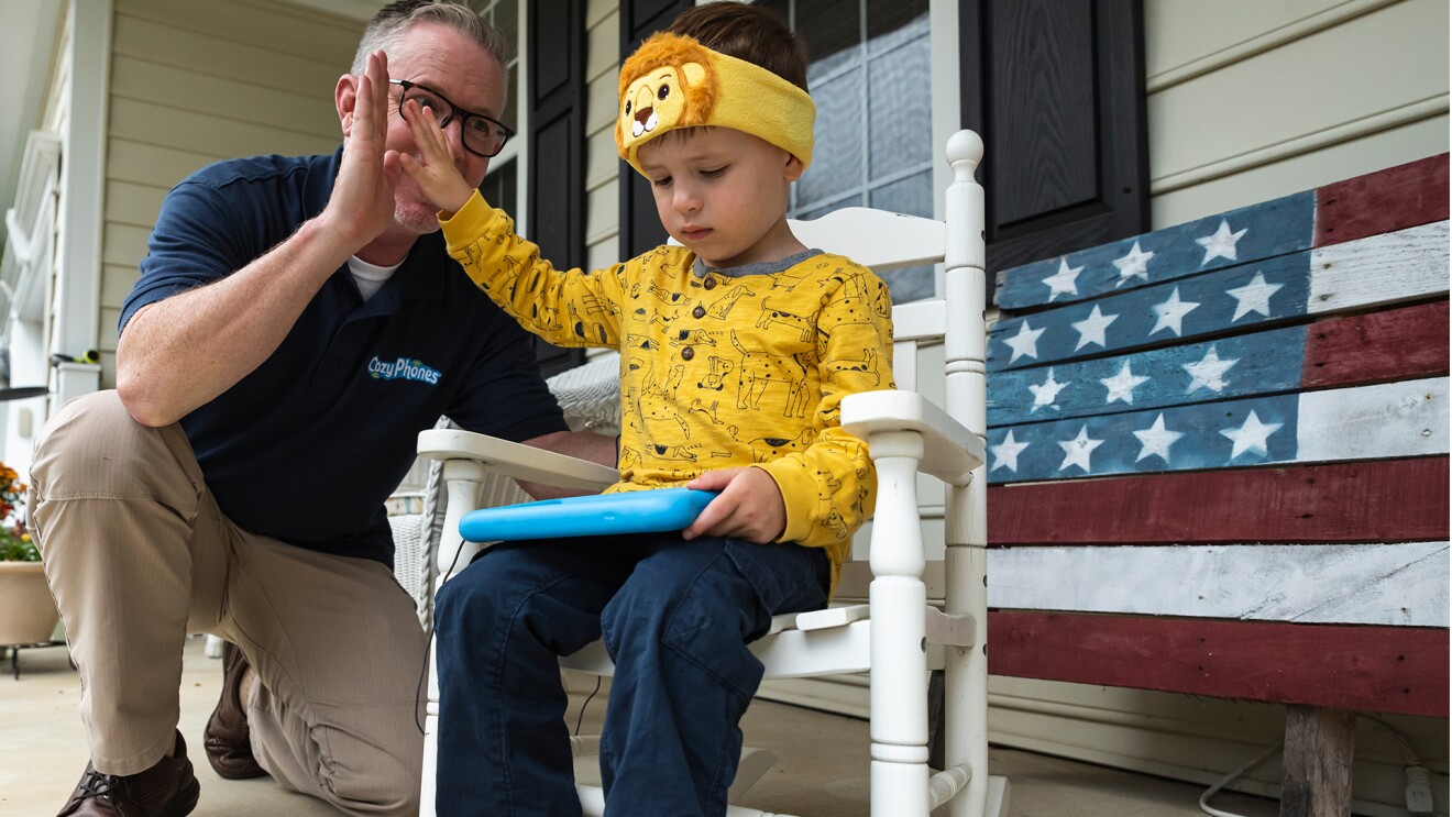 A man gives a high-five to a child sitting in a rocking chair.