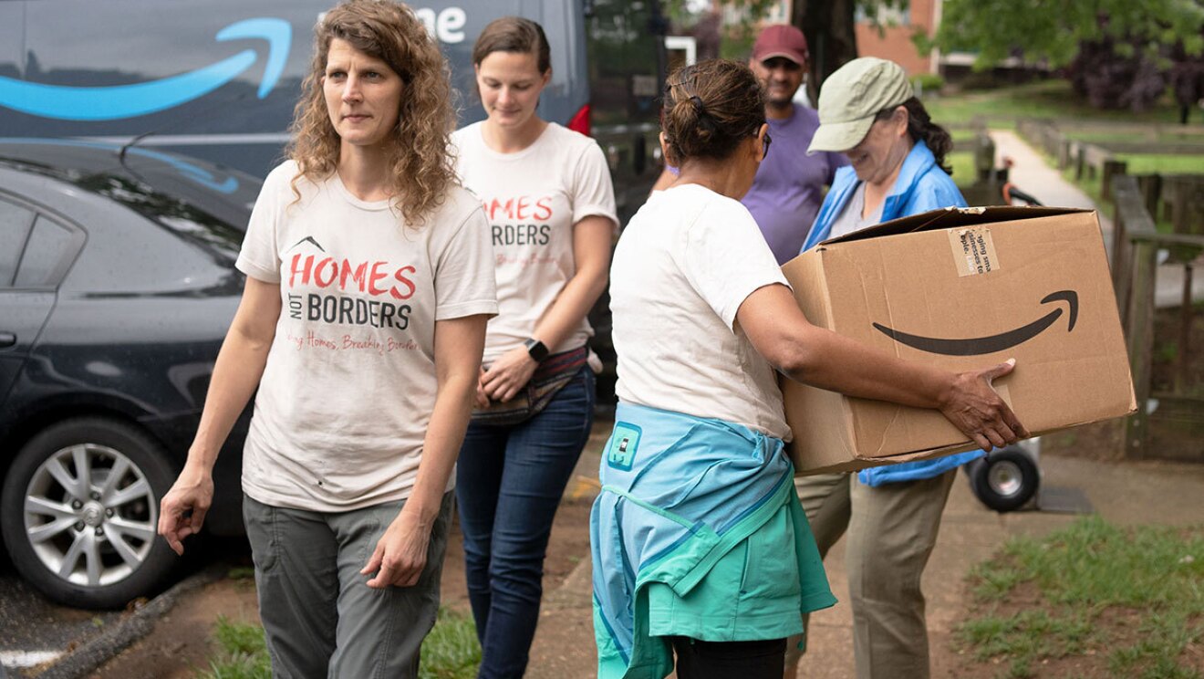 Volunteers and Amazon employees load up Amazon delivery vans with essential furniture and household products.