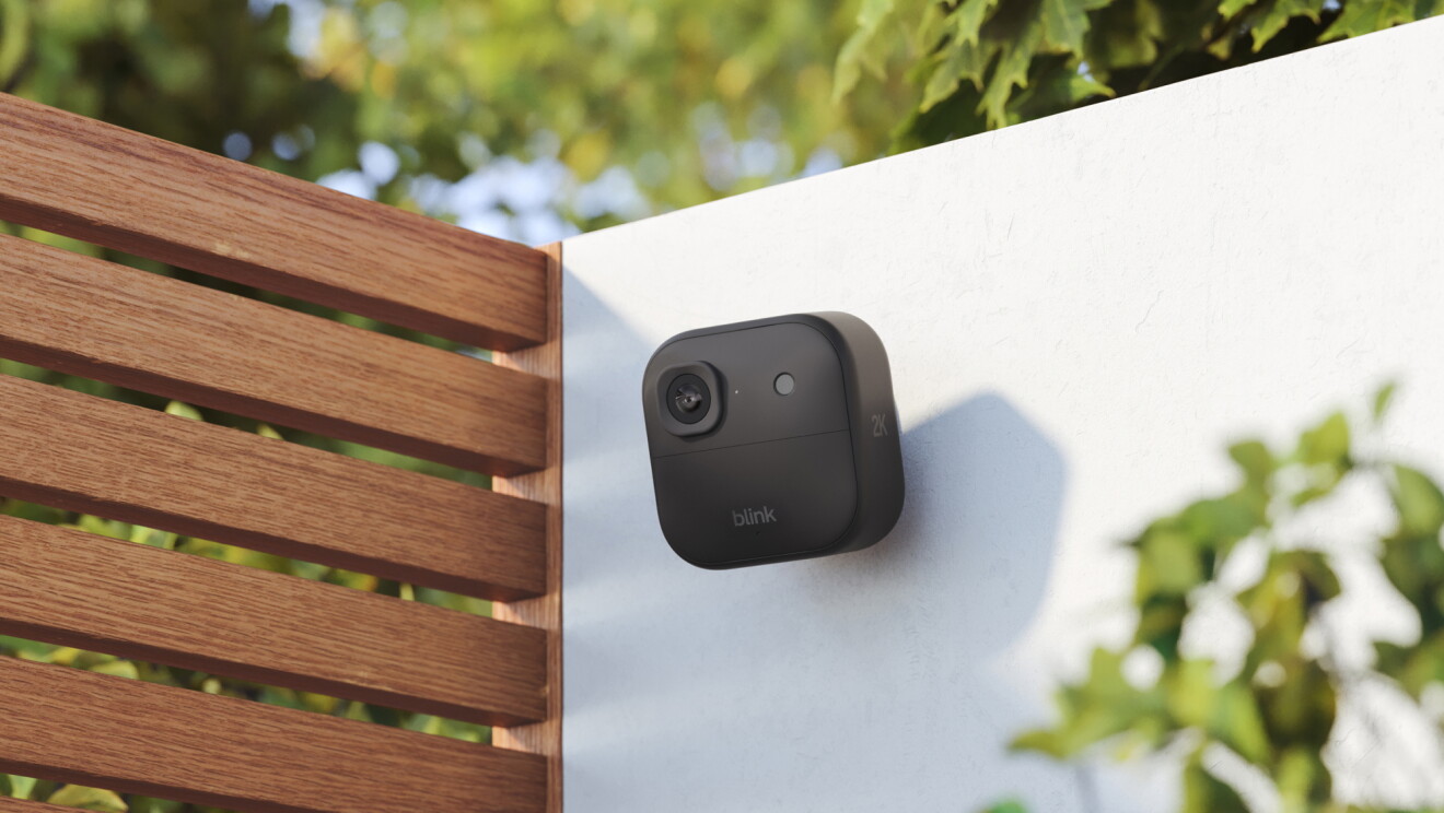 Blink camera secured to a white wall surrounded by greenery