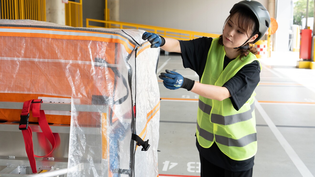 荷台に積まれた商品入りのボックスをベストを着た女性が取り付けている