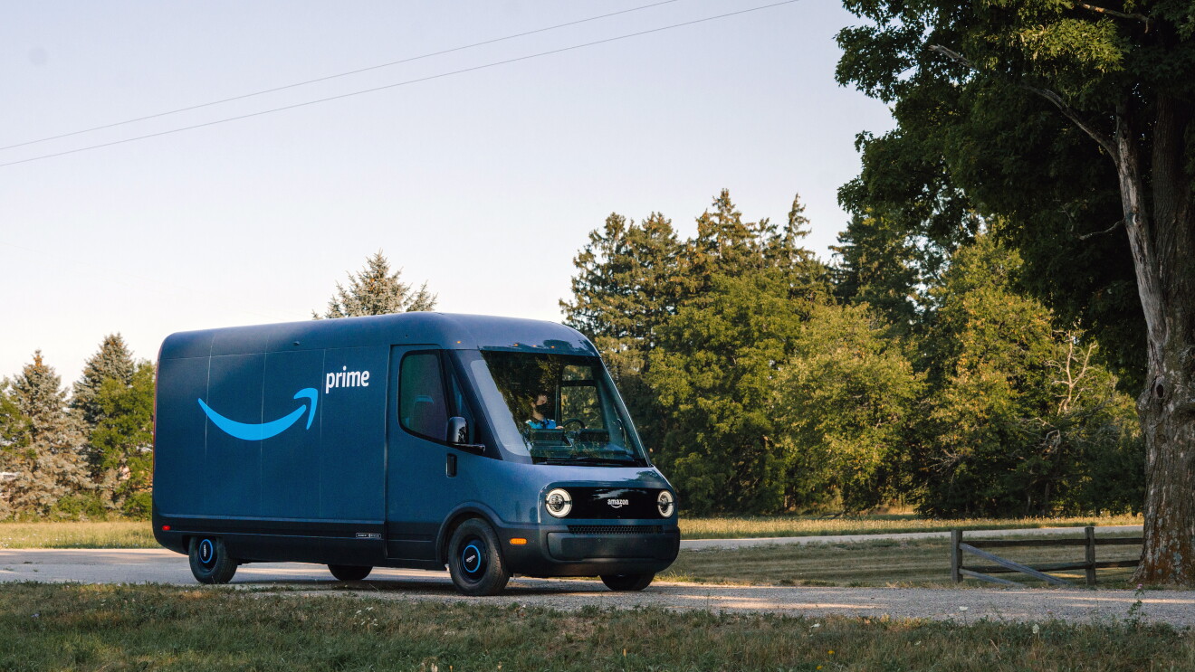 Furgone elettrico Rivian in una strada di campagna. Il furgone è blu e sulla fiancata ha il logo smile di Amazon e la scritta 'Prime'