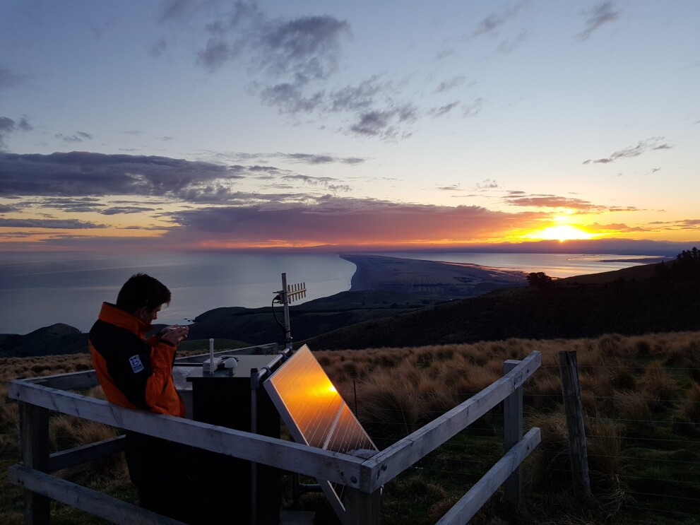 GeoNet field operations technician aligning an antenna with a compass at a monitoring site on Kaitorete Spit, Banks Peninsula, New Zealand. Conrad Burton, GNS Science.