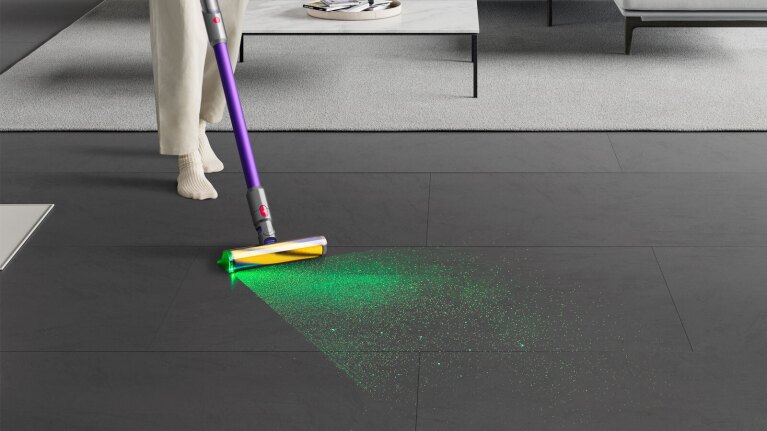 A person uses a Dyson vacuum to pick up green dust off the floor.