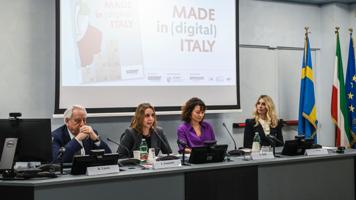Conferenza stampa di presentazione di Made in Digital Italy. Al tavolo sono sedute 4 persone. Sulla destra si vedono le bandiere dell'Italia e dell'UE. 