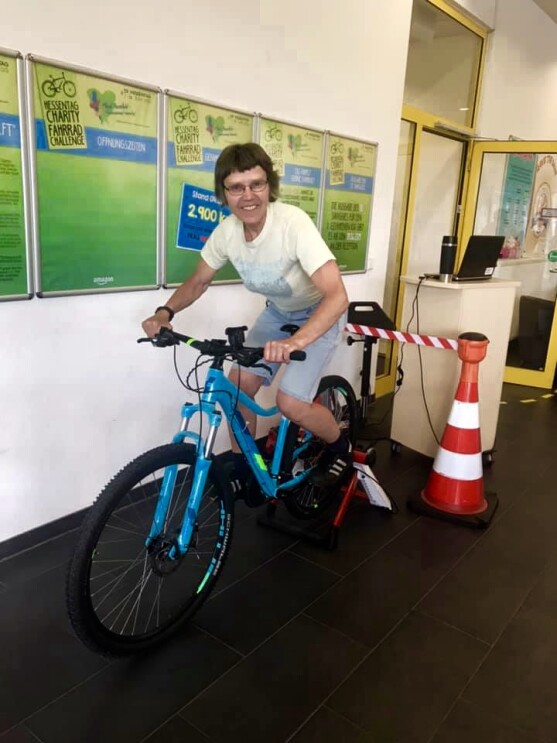 Eine braunhaarige Frau sitzt auf einem Fitnessrad. Sie trägt eine Brille und lächelt.