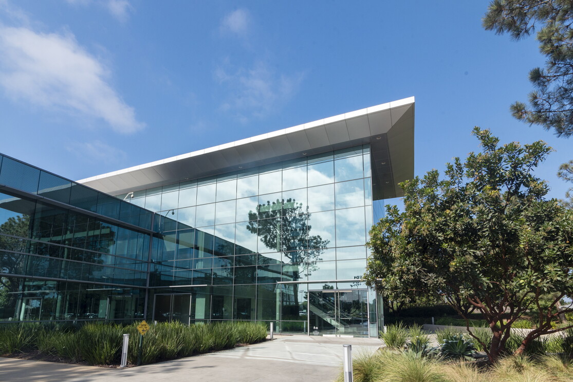 The exterior of a building, built of reflective glass, surrounded by grasses and trees.