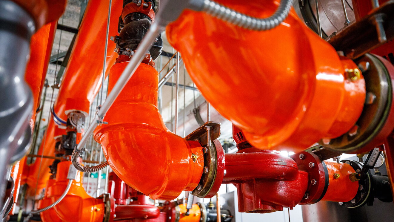 Three bright orange steam pipes are seen in a mechanical room under the Westin Seattle.
