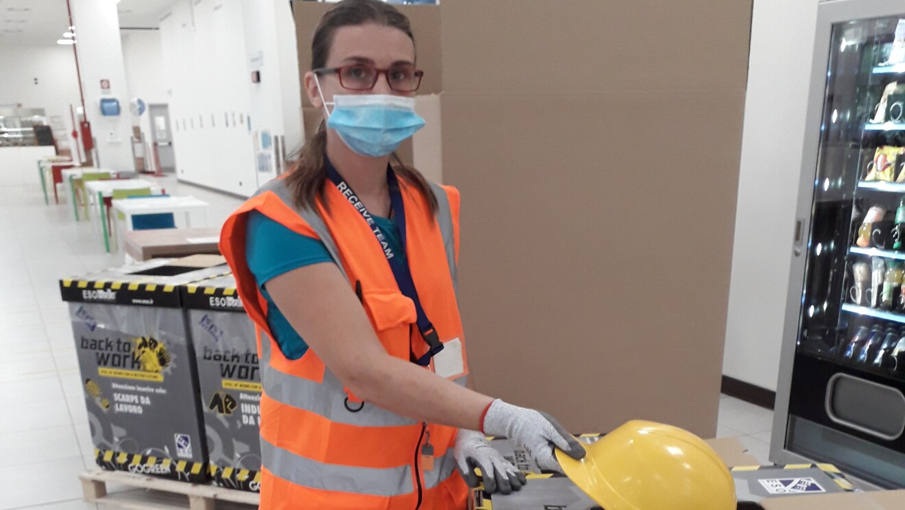 Un'operatrice di magazzino sta introducendo un caschetto da lavoro giallo all'interno di una scatola dedicata al riciclo degli indumenti da lavoro.