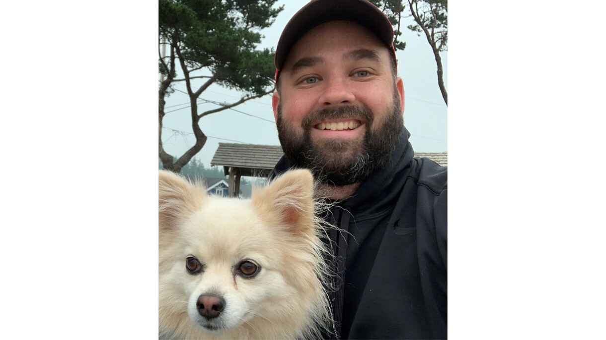 An image of a man smiling for a photo outside of his home. It is a selfie photo. 