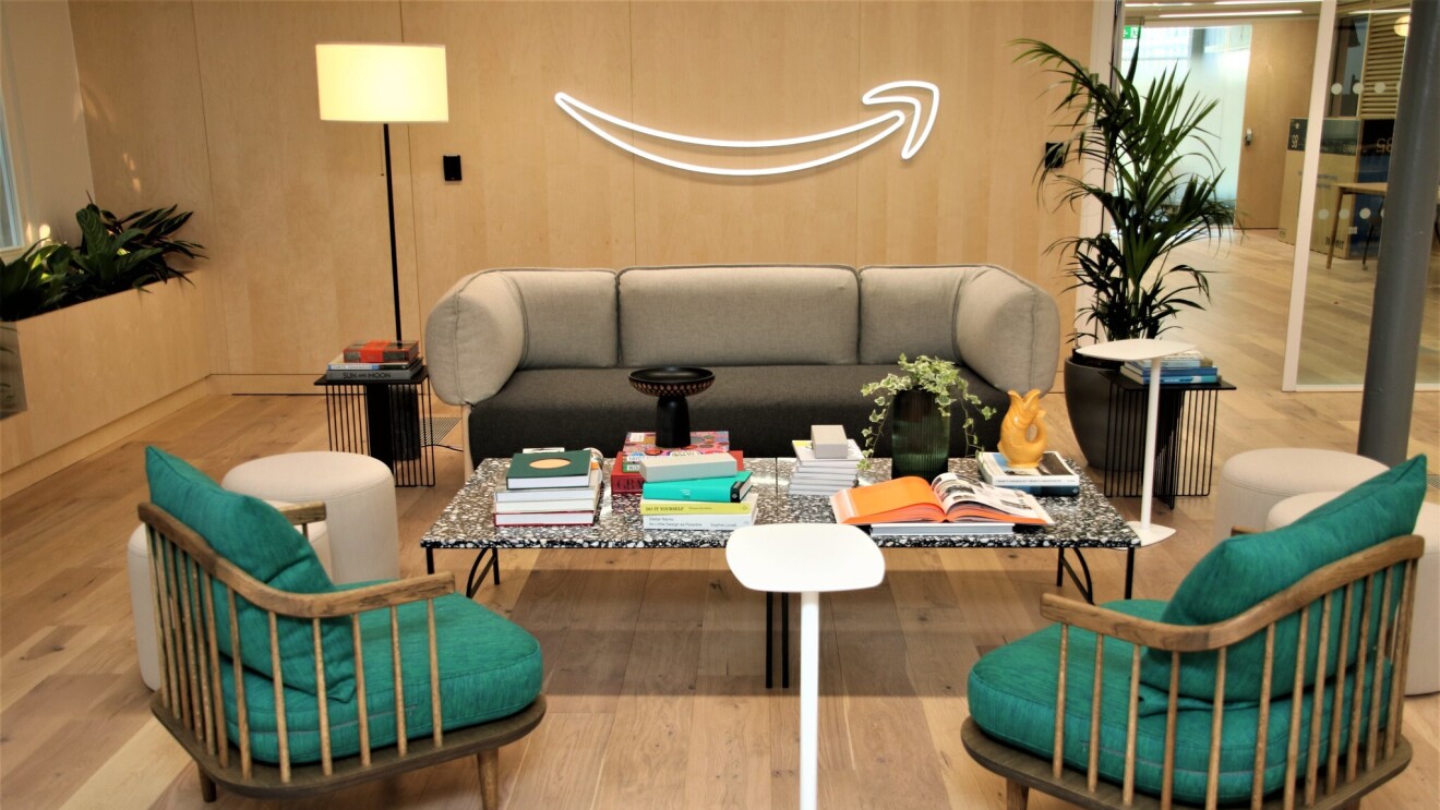 A view of the sitting area in the Amazon Manchester head office. There is a sofa and two armchairs surrounding a table which is covered in books, plants and ornaments.