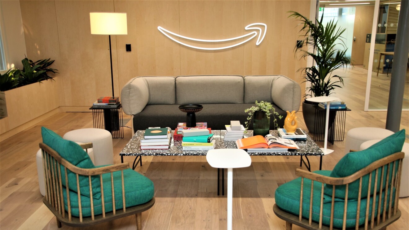 A view of the sitting area in the Amazon Manchester head office. There is a sofa and two armchairs surrounding a table which is covered in books, plants and ornaments. 