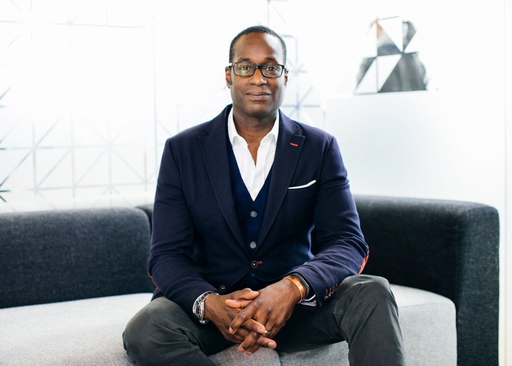 Oz Alashe dressed in a smart suit and sat on a sofa 