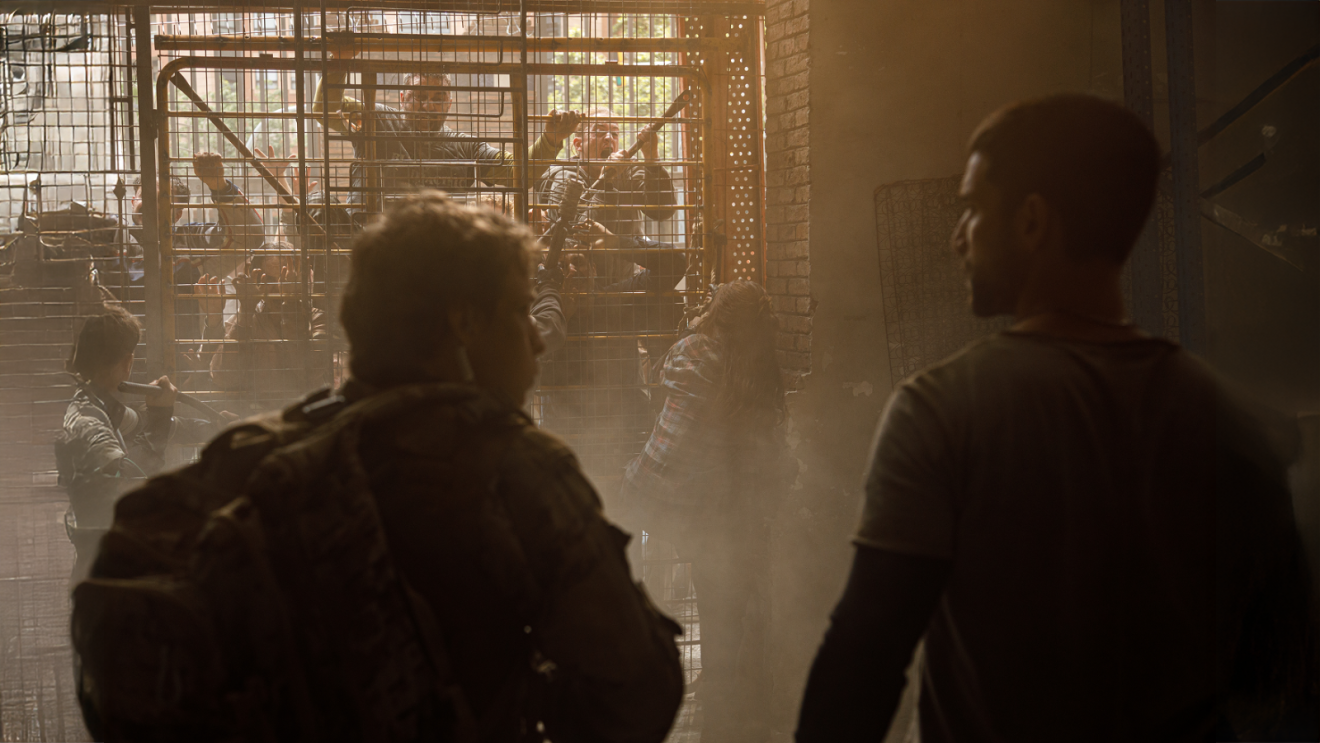 the backs of two men who face the a fence where people are trying to climb in