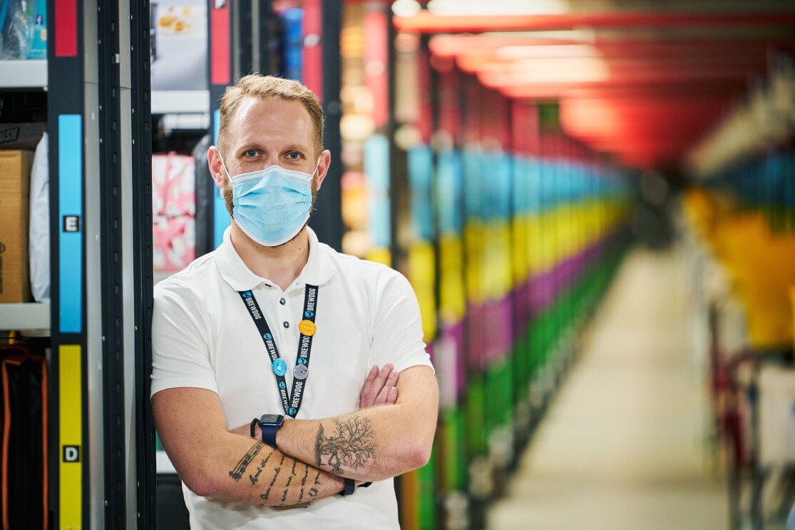 Craig Urquhart, Operations Manager at Amazon's fulfilment centre in Dunfermline, pictured cross-armed with colourful aisles blurred in the background