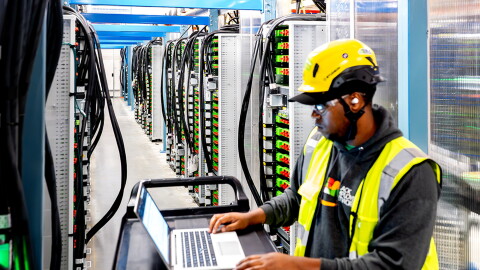 A data center technician working on a laptop device within a server room.