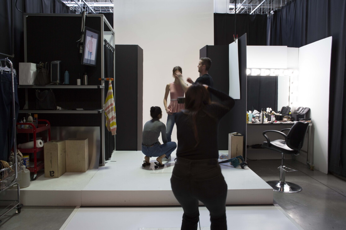 Two assistants, one male and one female, assist a model during an Amazon Fashion shoot. The photographer, who is silhouetted, is in the foreground.